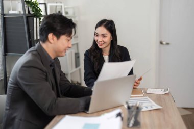 Bir erkek ve kadın takım üyesi, çağdaş bir ofiste takım çalışması sergileyen bir dizüstü bilgisayarla ve belgelerle mali raporları analiz ediyor..