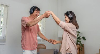 Yaşlı bir çift neşeyle dans ediyor ve el ele tutuşuyor kulaklıkla müzik dinliyor, sıcak bir ev ortamında sevgi ve bağlantıyı kutluyor..