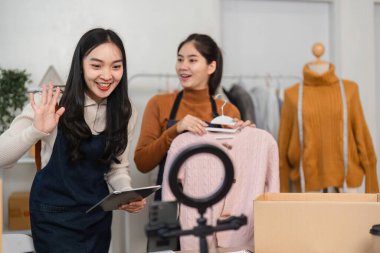 İki kadın online satışlar için giysi ürünleri sunarak yaratıcılıklarını ve moda girişimciliğindeki işbirliklerini sergilediler..