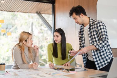 Çağdaş bir ofis ortamındaki bir masada tasarım materyallerini analiz eden çeşitli bir ekip odaklanmış bir tartışmaya girişti..