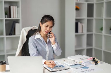 Kendini işine adamış bir finans işçisi, bir telefon görüşmesinde mesleki bir ortamda birden fazla görev içeren çizelgeleri ve verileri gözden geçirir..