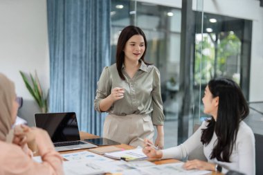Bir ofis ortamında çeşitli kadın grupları, toplantı sırasında mali veri ve grafikleri gözden geçirir..