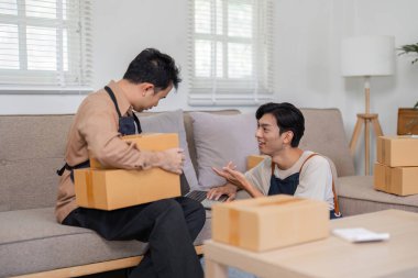 In a cozy living room, two online sellers collaborate on packaging and delivery methods, surrounded by boxes and a laptop. clipart