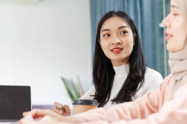 Genç bir Asyalı kadın aktif olarak bir toplantıya katılıyor, iş arkadaşlarıyla işbirliği ve bağlılık gösteriyor.