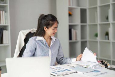 Bir finans işçisi, çağdaş bir çalışma alanında örgütlenme ve analize odaklandığını gösteren belgeleri ve verileri masasında gözden geçirir..