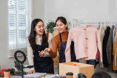 İki hevesli girişimci online giyim işlerini tartışırken, takım çalışmalarını ve yaratıcılıklarını ön plana çıkararak pembe bir kazak sunuyorlar..