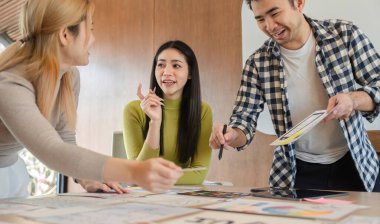 Çeşitli profesyonellerden oluşan bir grup, bir ofis masası etrafında tartışırken bir tasarım projesinde fikir paylaşımı ve işbirliği yapıyorlar..