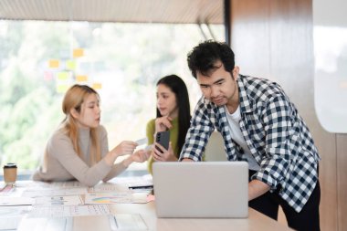 Dizayn materyallerini inceleyen ve işbirliği yapan çeşitli bir ekip, bir üye dizüstü bilgisayar kullanırken, diğerleri modern ofis ortamında veri sağlıyor.