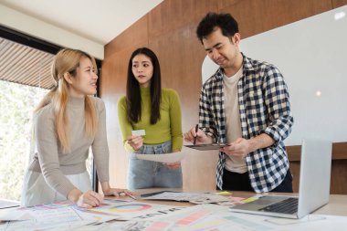 Yaratıcı bir tasarım projesinde işbirliği yapan, fikirleri tartışan ve modern ofis çalışma alanında dijital araçlar kullanan çeşitli profesyonellerden oluşan bir grup..