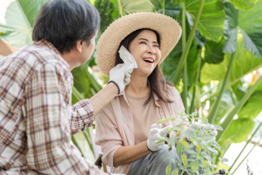 Yaşlı bir Asyalı kadın, yemyeşil bahçeyle çevrili bahçelerini severek seyrederken partnerlerinin yüzüne dokunuyor..