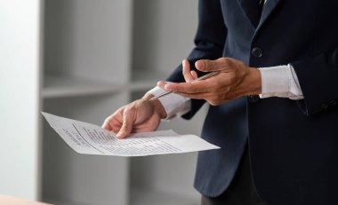 Bir avukat elinde kalemle kontrat belgelerini incelerken modern ofis ortamında profesyonelliğini sergiliyor..