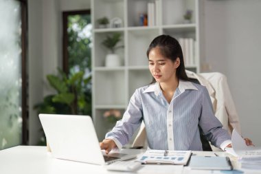 Bir finans uzmanı, şık bir ofis ortamında profesyonelliği vurgulayarak, veri analizi ve belge yönetimi üzerinde gayretle çalışır..