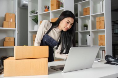 Bir iş kadını modern girişimciliğin sergilendiği şık bir çalışma alanındaki envanteri yönetmek için dizüstü bilgisayar ve defter kullanır..