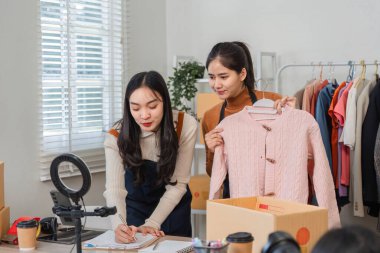 İki genç kadın online giyim mağazalarını yönetiyor, pazarlama fikirlerini beyin fırtınası yaparken mor bir tişört sergiliyorlar, yaratıcılığı ve takım çalışmasını somutlaştırıyorlar..