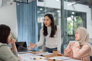Bir grup farklı kadın, çağdaş bir ofis ortamında üretken bir toplantıya katılıyor, fikirleri ve stratejileri paylaşıyor..