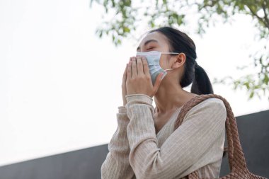 Yüzüne maske takan genç bir kadın, hava kirliliği ve hava kalitesi hakkındaki endişelerini dile getiriyor..