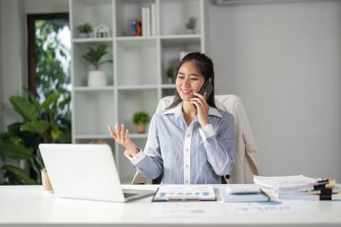 Bir finans uzmanı telefon görüşmesi yaparken gülümser, modern ofis ortamında finansal stratejileri tartışır, profesyonelliği ve bağlılığı gösterir.