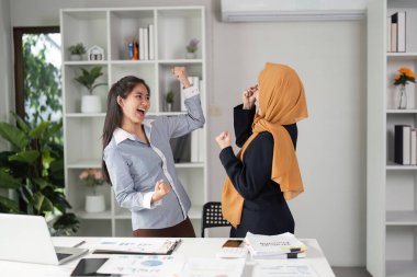 İki farklı iş kadını modern bir ofiste başarılarını sevinçle kutluyor, takım çalışması ve heyecan sergiliyorlar..