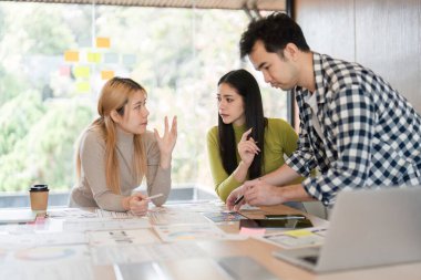 Çeşitli takım üyeleri parlak bir ofis alanında materyalleri incelerken aktif olarak tasarım projelerini tartışıyor ve işbirliği yapıyorlar..
