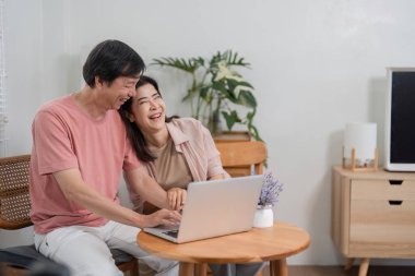 Neşeli yaşlı bir çift birlikte oturur, güler ve anı paylaşır. Bu arada modern yaşam alanlarında dizüstü bilgisayar kullanırlar..