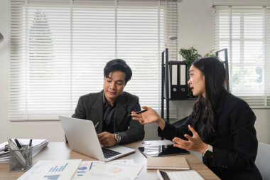 Verileri analiz eden ve iyi aydınlatılmış modern bir ofiste finansal stratejiler hakkında bir tartışmaya giren iki farklı profesyonel.