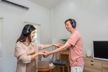 Orta yaşlı neşeli bir çift oturma odalarında kulaklık takıp dans ediyor, müzik dinliyor ve birbirlerine eşlik ediyorlar..