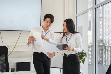 İki meslektaş birlikte vergi raporlarını analiz ediyor, modern bir çalışma alanında takım çalışması ve profesyonel katılımı vurguluyor.