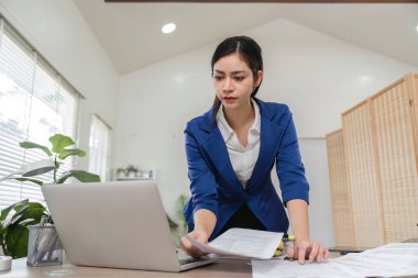 Profesyonel bir muhasebeci, vergi dosyalarında doğruluğu sağlamak için bilgisayarla çalışırken mali belgeleri gözden geçirir..