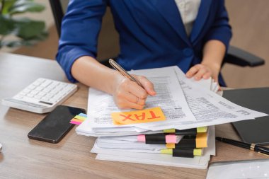 Bir muhasebeci, mali dosyalamaya hazırlanmak için hesap makinesi kullanırken vergi belgeleri üzerine yazar.
