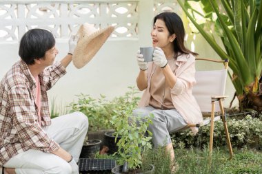 Bahçelerinde çeşitli bir çift, neşeli bir an paylaşıyorlar. Biri elinde bir hasır şapka, diğeri ise bitkilerle çevrili kahveyi yudumluyor..