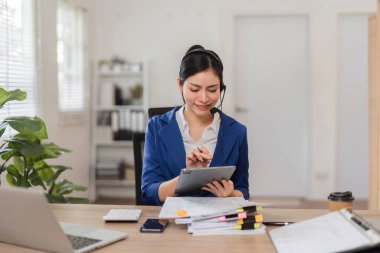Odaklanmış bir muhasebeci müşterilerine yardımcı olmak için bir tablet ve evrak işlerinden faydalanıyor, rahat bir ofiste modern finans uygulamalarını vurguluyor.