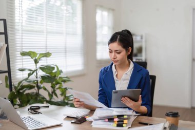 Bir muhasebeci, tablet kullanırken, organizasyonu gösterirken ve profesyonel bir ortamda odaklanırken mali evrakları inceler..