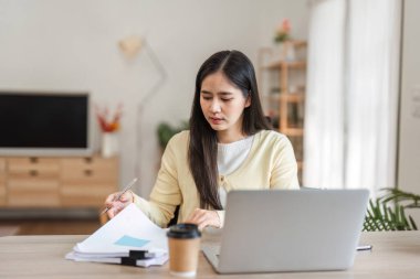 Evrakları inceleyen ve bilgisayarını rahat bir ofiste çalışırken notlar alan odaklanmış genç bir kadın verimli bir atmosferi vurguladı..