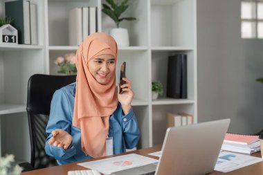 Kendine güvenen, tesettürlü bir Müslüman kadın şık bir ofis ortamında telefonla konuşuyor..