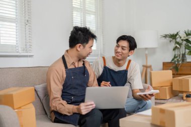 İki genç Asyalı girişimci rahat ofislerinde iş birliği yapıyor, planlarını gözden geçiriyor ve nakliyeye hazır paketlerle e-ticaret işlerini tartışıyorlar..