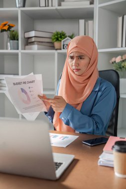 Modern ofis ortamındaki bir dizüstü bilgisayardaki incelemesi sırasında bütçeli pasta grafiğini sorgulayan tesettürlü kadın muhasebeci şaşırmış görünüyor..
