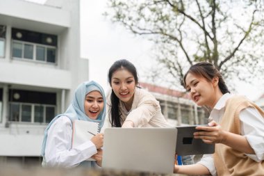 Üç farklı kız öğrenci heyecanlı bir şekilde bir projeyi tartışırken açık havada dizüstü bilgisayarı gösteriyorlar, kampüs ortamında işbirliği ve bağlılık gösteriyorlar..