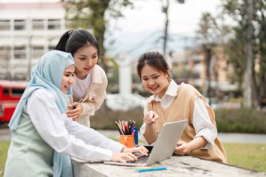 Çeşitli bir grup kadın bir dizüstü bilgisayarla uğraşıyorlar, bir üniversite ortamında neşeli bir şekilde iş birliği yapıyorlar, fikirleri paylaşıyorlar ve birlikte öğreniyorlar..