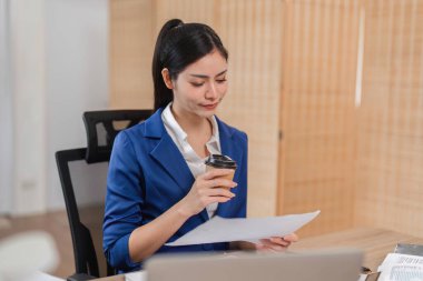 Çalışkan bir işkadını mali belgeleri analiz eder ve kahveden zevk alır, vergi hazırlama konusundaki kararlılığını vurgular.