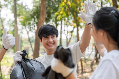 Neşeli genç bir adam topluluk temizliği sırasında elini kaldırıyor, takım çalışması ve çevre sorumluluğunu vurguluyor..