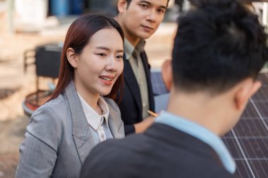 Bir iş kadını, meslektaşları güneş enerjisi teknolojisi, takım çalışması ve sürdürülebilirlikteki yenilikleri tartışırken gülümsüyor.