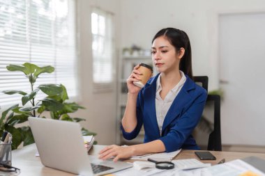 Bir iş kadını, masasında mali görevler üzerinde çalışırken kahve yudumlamak, iş ve rahatlamayı dengelemek için ara verir..