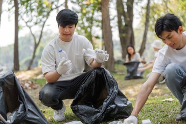 İki genç gönüllü, bir parkı temizlerken plastik şişeleri sınıflandırıyor, takım çalışması ve çevre bakımını vurguluyor.