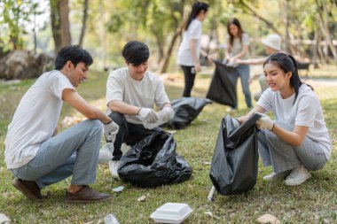 Bir grup gönüllü aktif olarak bir park temizliğinde çalışıyor, çöp topluyor ve takım çalışması ile sürdürülebilirliği destekliyor..