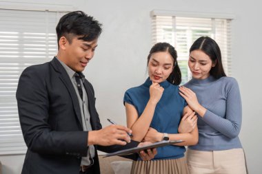 Bir emlakçı, iki potansiyel alıcının çağdaş bir oturma odasında dikkatle izlediği önemli bilgileri yazar..