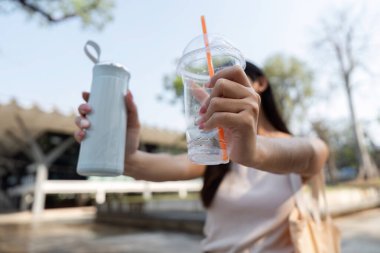 Bir kadın iki çevre dostu içecek konteynırını tutarken, açık havanın tadını çıkarırken sürdürülebilir bir yaşam tarzına olan bağlılığını vurguluyor..