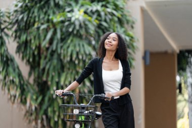 Genç kadın bisikletinin yanında duruyor, neşe saçıyor ve şehir ortamlarında sağlıklı, ekolojik bilinçli bir yaşam tarzını kucaklıyor..