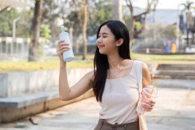 Genç bir kadın açık havayı seviyor, elinde tekrar kullanılabilir bir bardak tutarken parktaki çevre dostu yaşam tarzını gösteriyor..