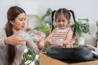 Kendini işine adamış bir anne, küçük kızını eğlenceli bir geri dönüşüm aktivitesine dahil eder ve ona evde plastik atıkların nasıl sınıflandırılacağını gösterir..