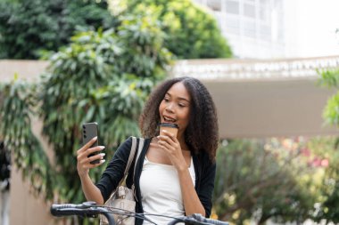 Bu görüntü, bir kadının gününü selfie ile belgelendirirken, hayat tarzı ve keyfine ışık tutarken kahvenin tadını çıkardığı canlı bir anı yakalıyor..